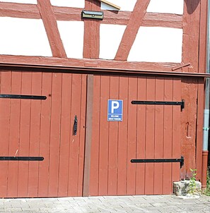 Une porte en bois rouge avec un panneau bleu portant la lettre « P », indiquant l’emplacement réservé au stationnement des visiteurs.
