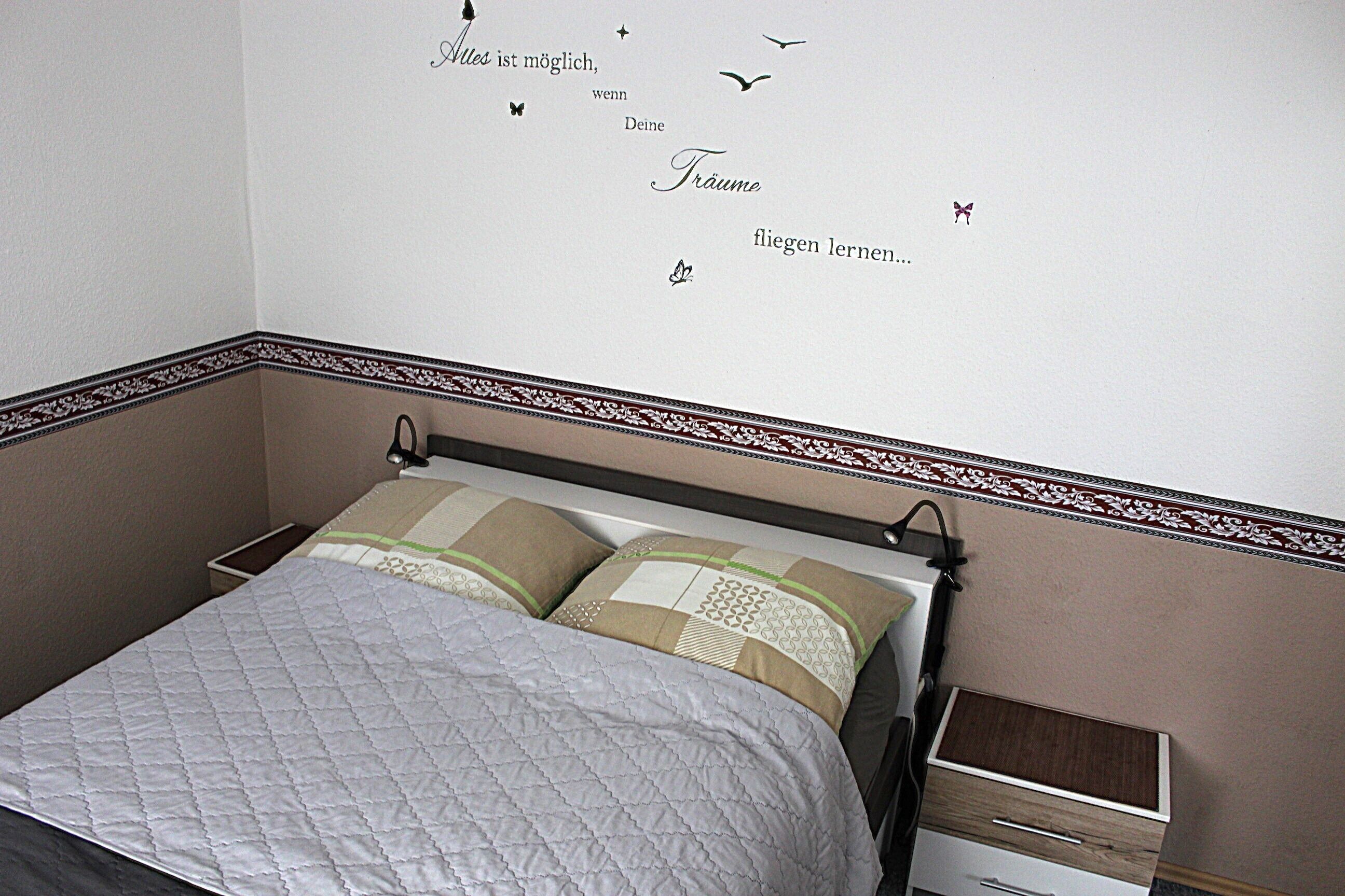 A bedroom with a bed, a nightstand, and a wall with decorative decals.
