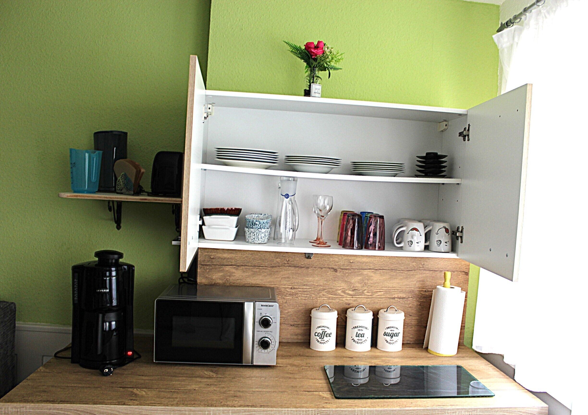 Eine Küche mit Mikrowelle, Kaffeemaschine sowie Zucker und Tee auf der Arbeitsfläche.
