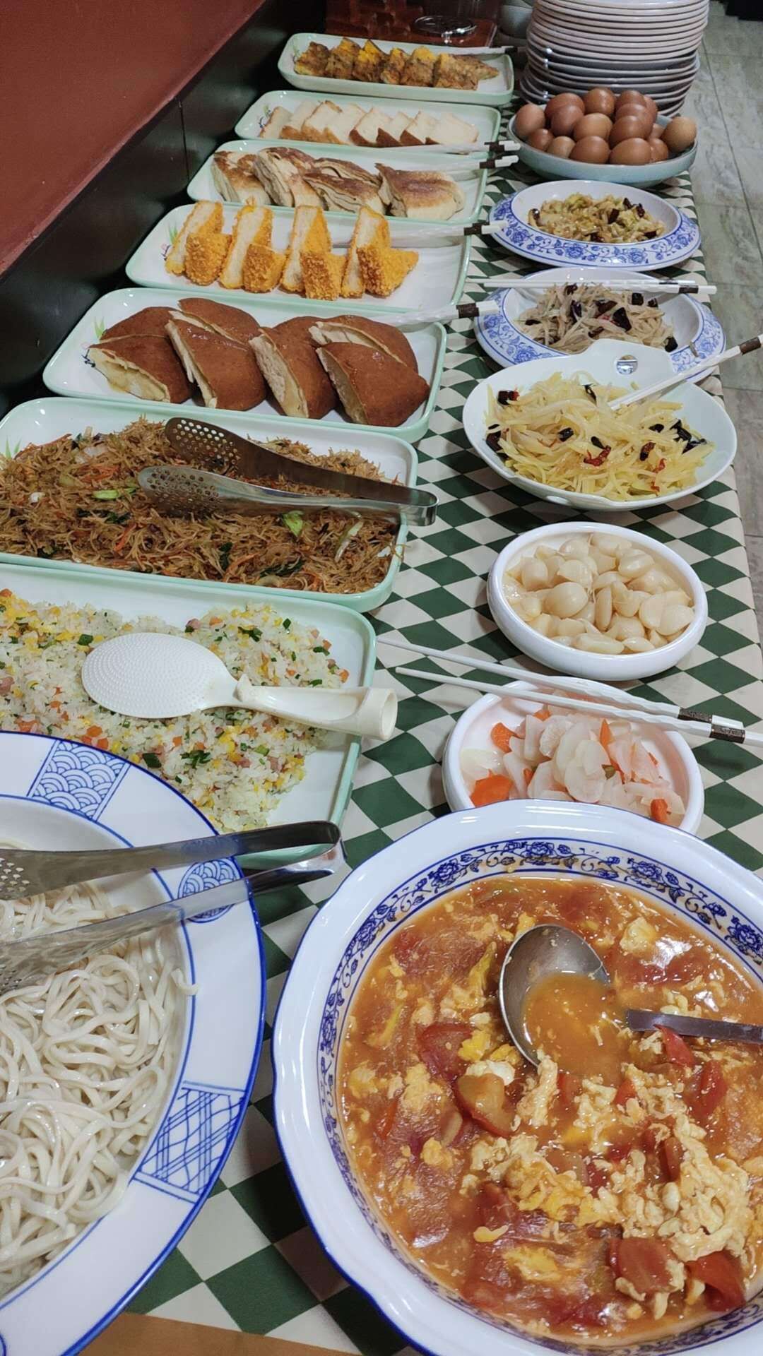 A buffet table with various dishes including fried rice, noodles, and a bowl of soup.