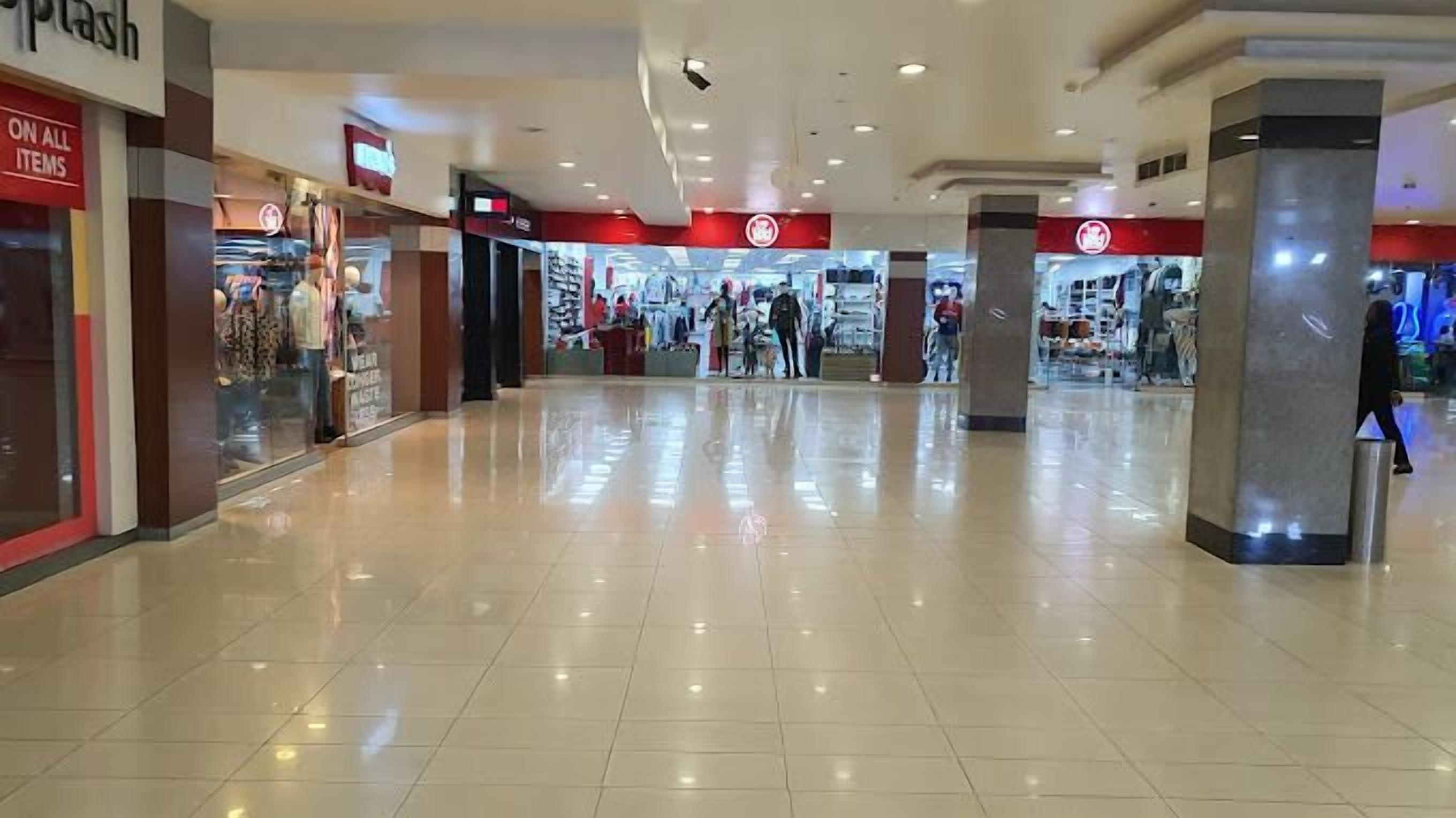 A spacious shopping mall corridor with a clean, tiled floor and a few shoppers.