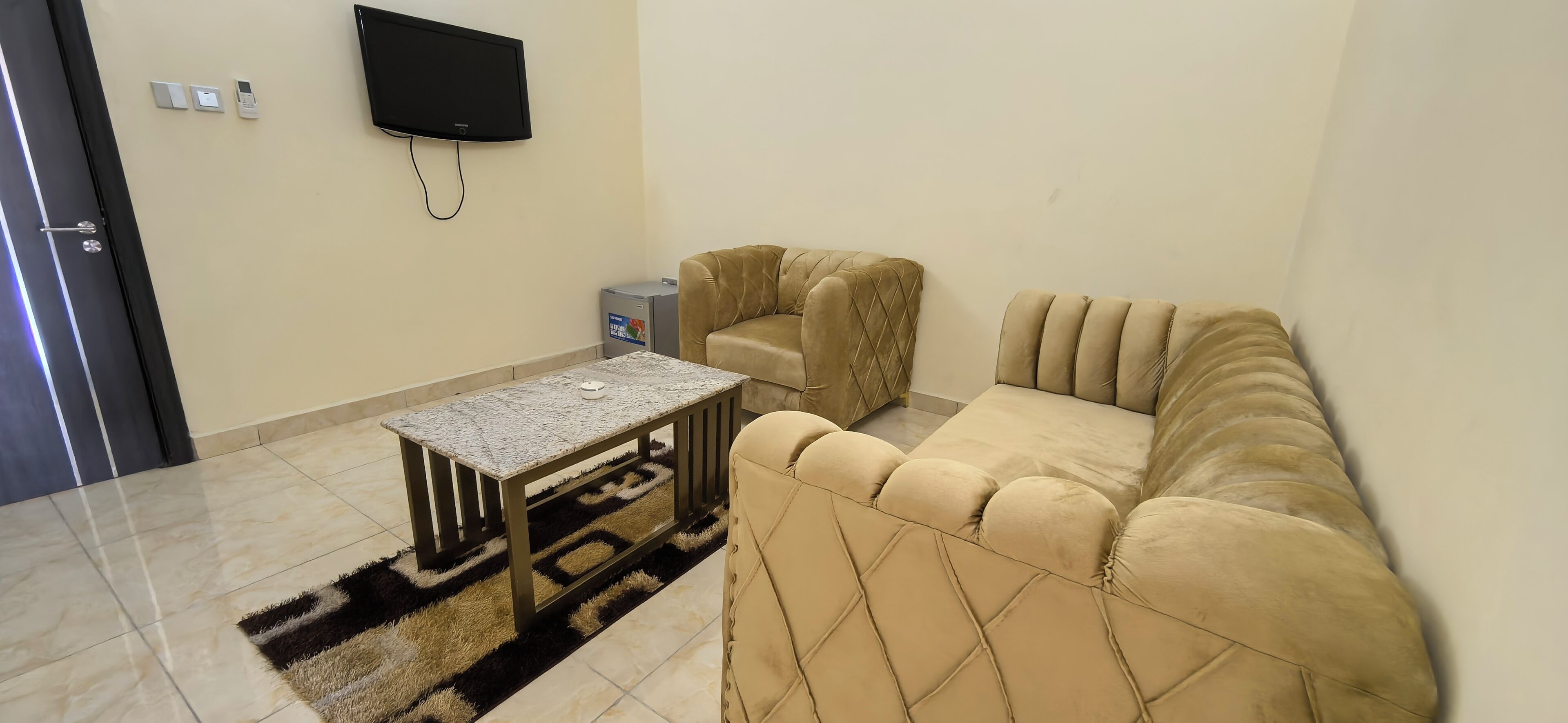 A living room with a beige sofa, a small coffee table, a TV mounted on the wall, and a small cabinet.