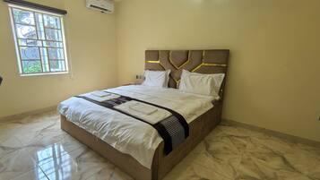 A hotel room with a bed, a chair, a window, and an air conditioning unit.