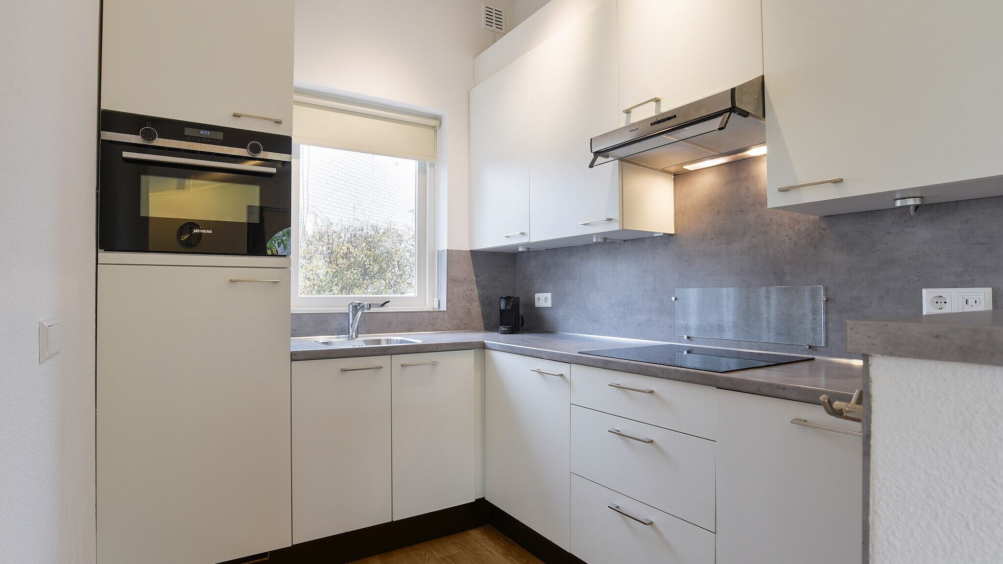 Eine moderne Küche mit weißen Schränken, einem eingebauten Backofen, einem Fenster und einer Kaffeemaschine.