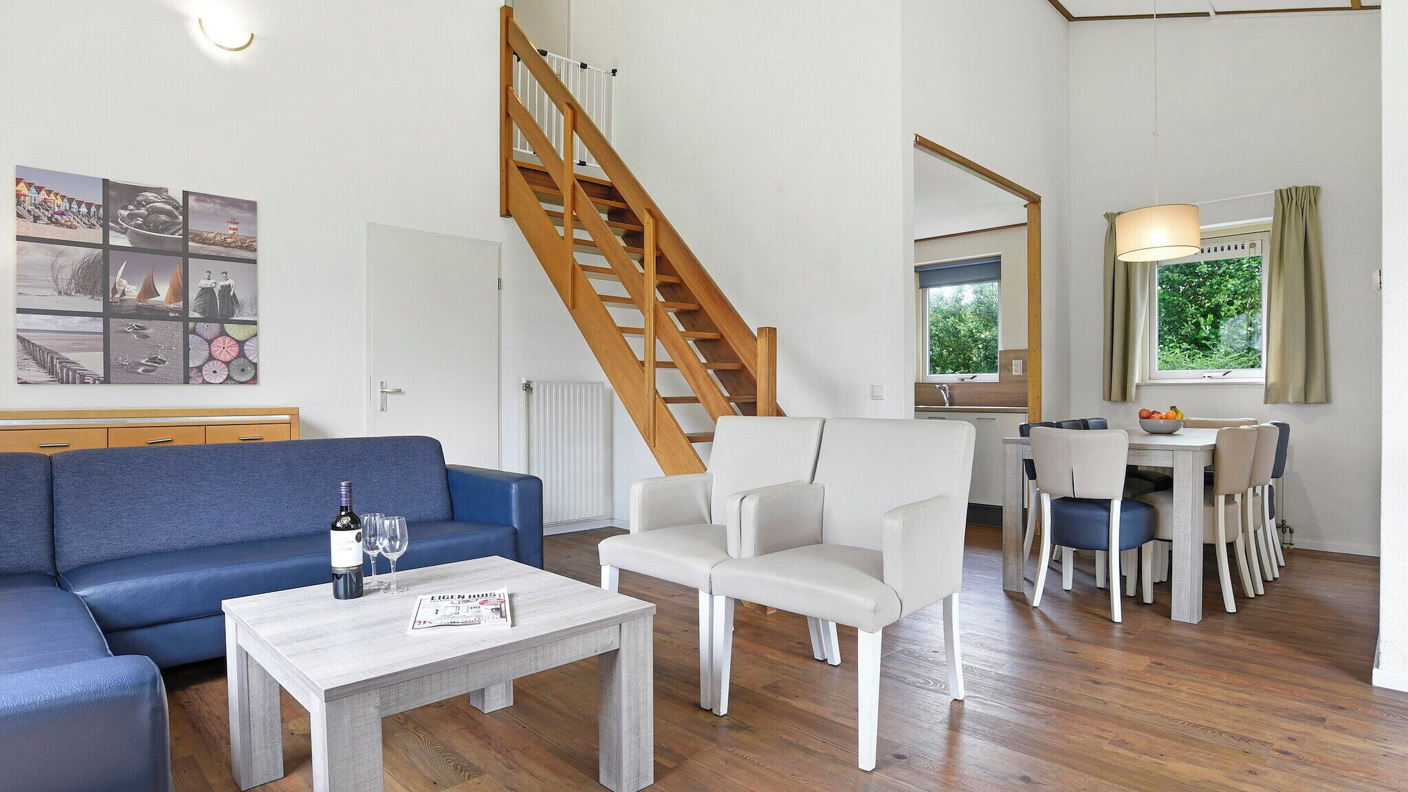 Ein modernes Wohnzimmer mit einem blauen Sofa, weißen Stühlen, einer Holztreppe und einem Essbereich mit Tisch und Stühlen.