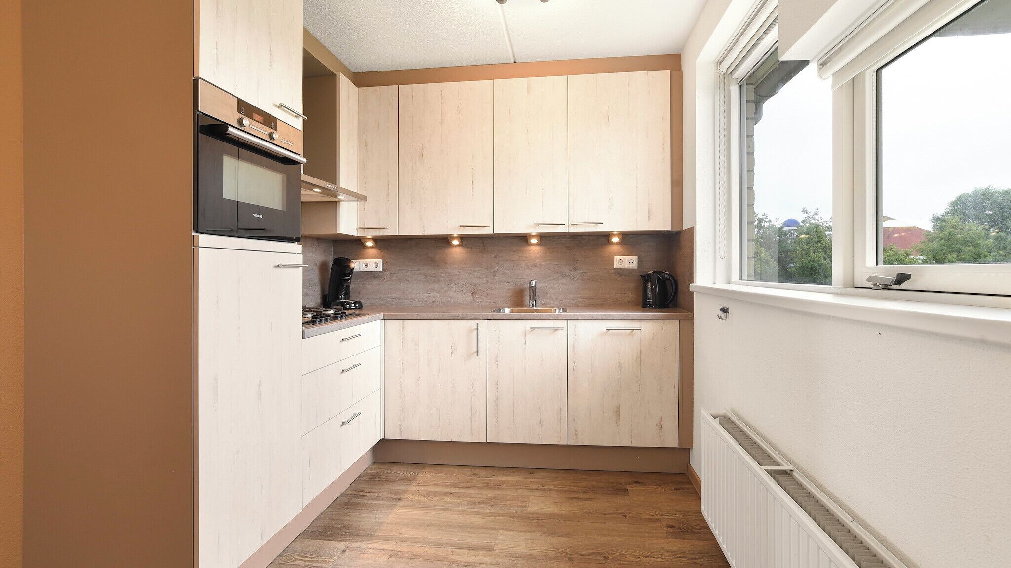 A narrow kitchen with wooden cabinets, a built-in oven, and a window providing a view of the outside.