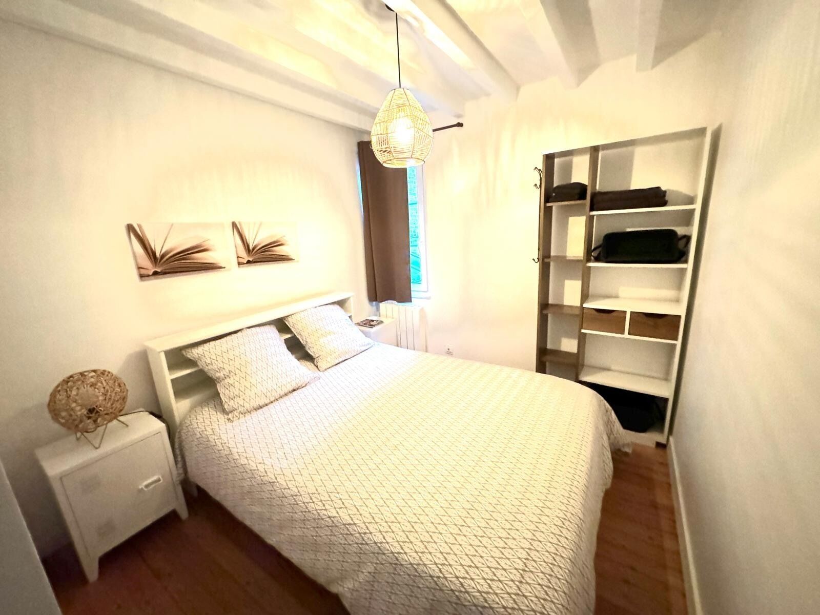 A bedroom with a bed, a nightstand, a hanging light fixture, a window with curtains, and a built-in wardrobe.