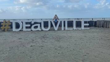 Ein Strand mit einem großen, weißen Schild, auf dem "DEAUVILLE" steht, und einem Holzzaun im Hintergrund.