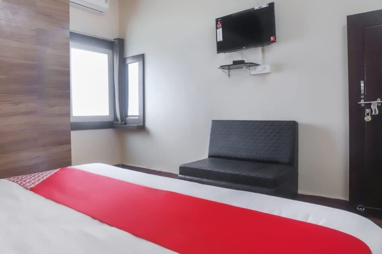 A hotel room with a bed, a television mounted on the wall, a window, and a door.