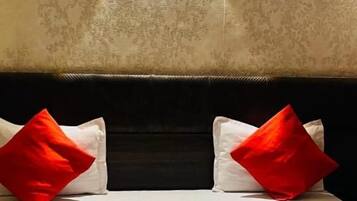A hotel room with a bed, red and white pillows, a red and white bedspread, a rolled towel, and two water bottles.