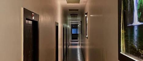 A long, narrow hallway with doors on both sides, recessed lighting, and a large framed picture on the right wall.