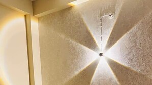 Ein Hotelzimmer mit einem großen Bett, rot-weißer Bettwäsche, einem schwarzen Kopfteil und einer strukturierten Wand mit einer Leuchte.