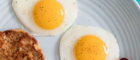 Dos huevos fritos soleados sobre un plato con una rebanada de tostada y una tira de tocino.