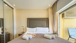 A hotel room with a large bed, a headboard, two bedside tables with lamps, a chair, and a window with curtains.