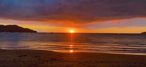 Een zonsondergang boven een strand met boten en een landschap in de verte.