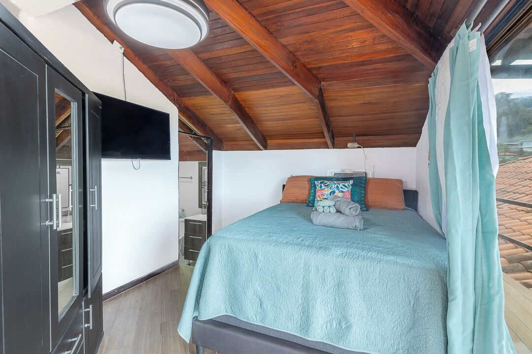 A bedroom with a bed, pillows, a TV, and a window.