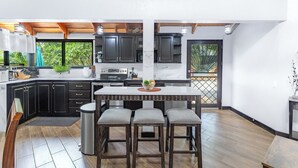 Una cocina moderna con armarios oscuros, una isla central con taburetes y vistas a zonas verdes.