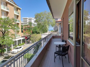 A balcony with a table and chairs, overlooking a street with parked cars and buildings.