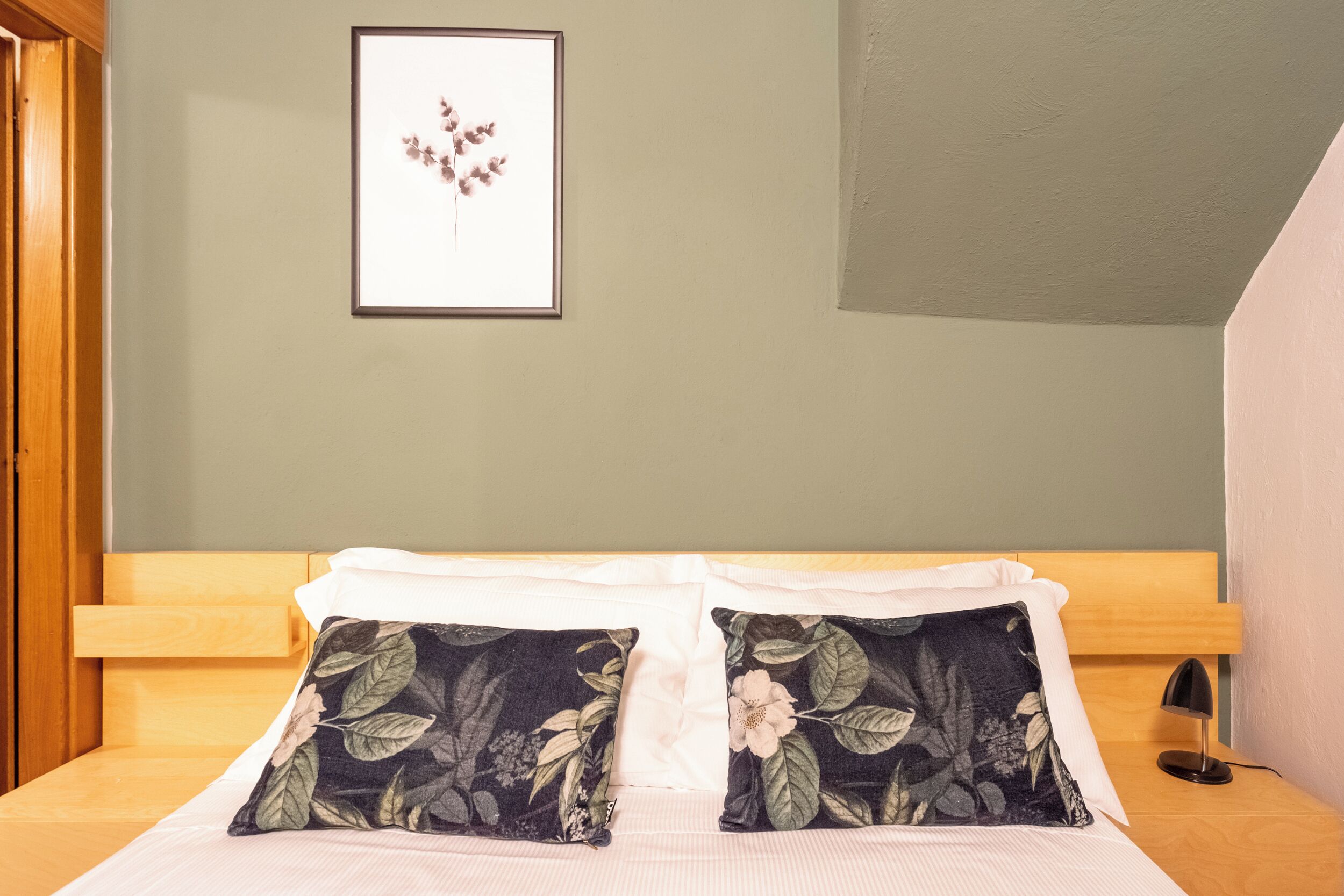Una cama bien hecha, con almohadones florales, un cuadro en la pared y un cabecero de madera.