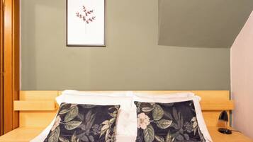 Una cama bien hecha, con almohadones florales, un cuadro en la pared y un cabecero de madera.