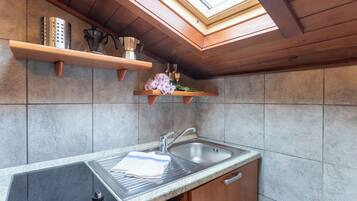 Een keuken met een inbouwfornuis, een spoelbak, houten kastjes en een dakraam boven het aanrecht.