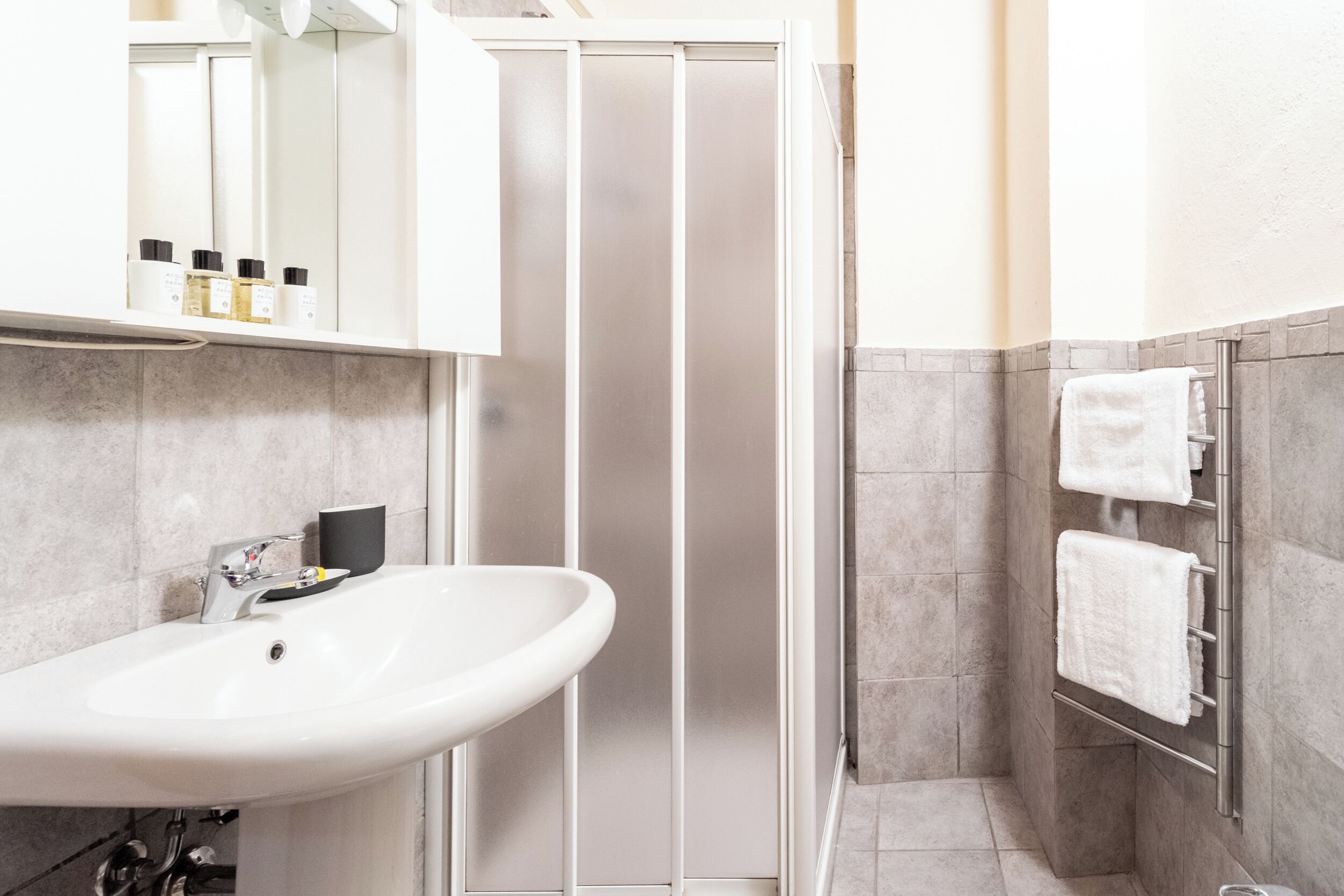 Un bany modern amb un lavabo blanc, un mirall i una dutxa tancada.