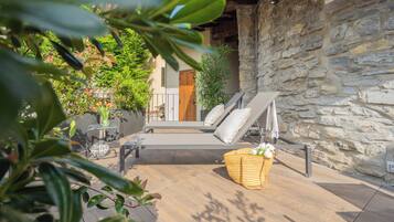Un área de lounge al aire libre con paredes de piedra, una terraza de madera, una cesta de mimbre y una silla de descanso.