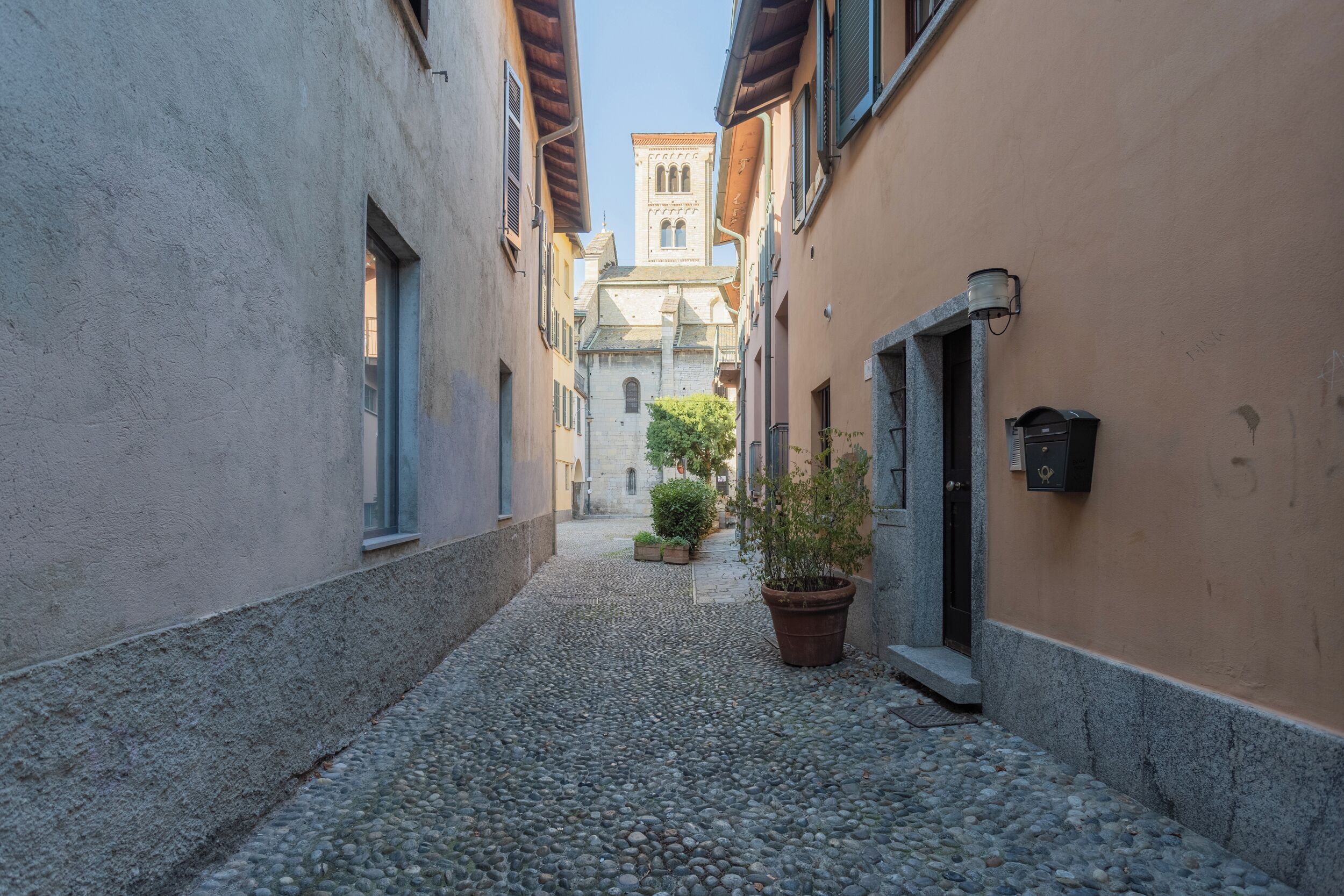 A narrow cobblestone alley flanked by buildings with a church tower in the distance.