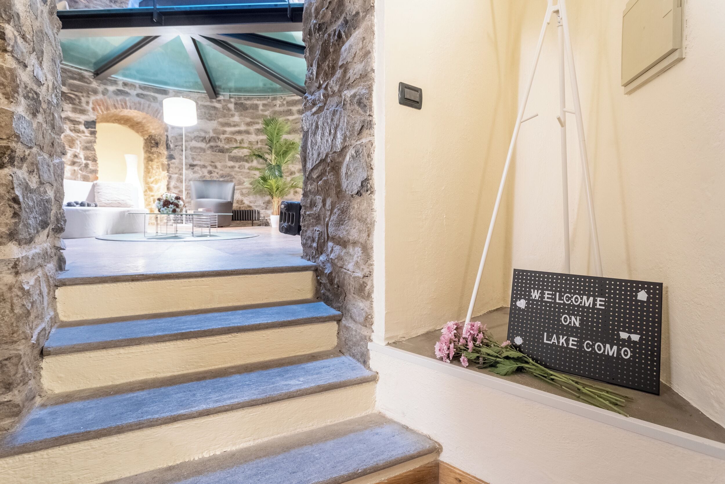 A staircase leading to a stone-walled room with a 'Welcome on Lake Como' sign.