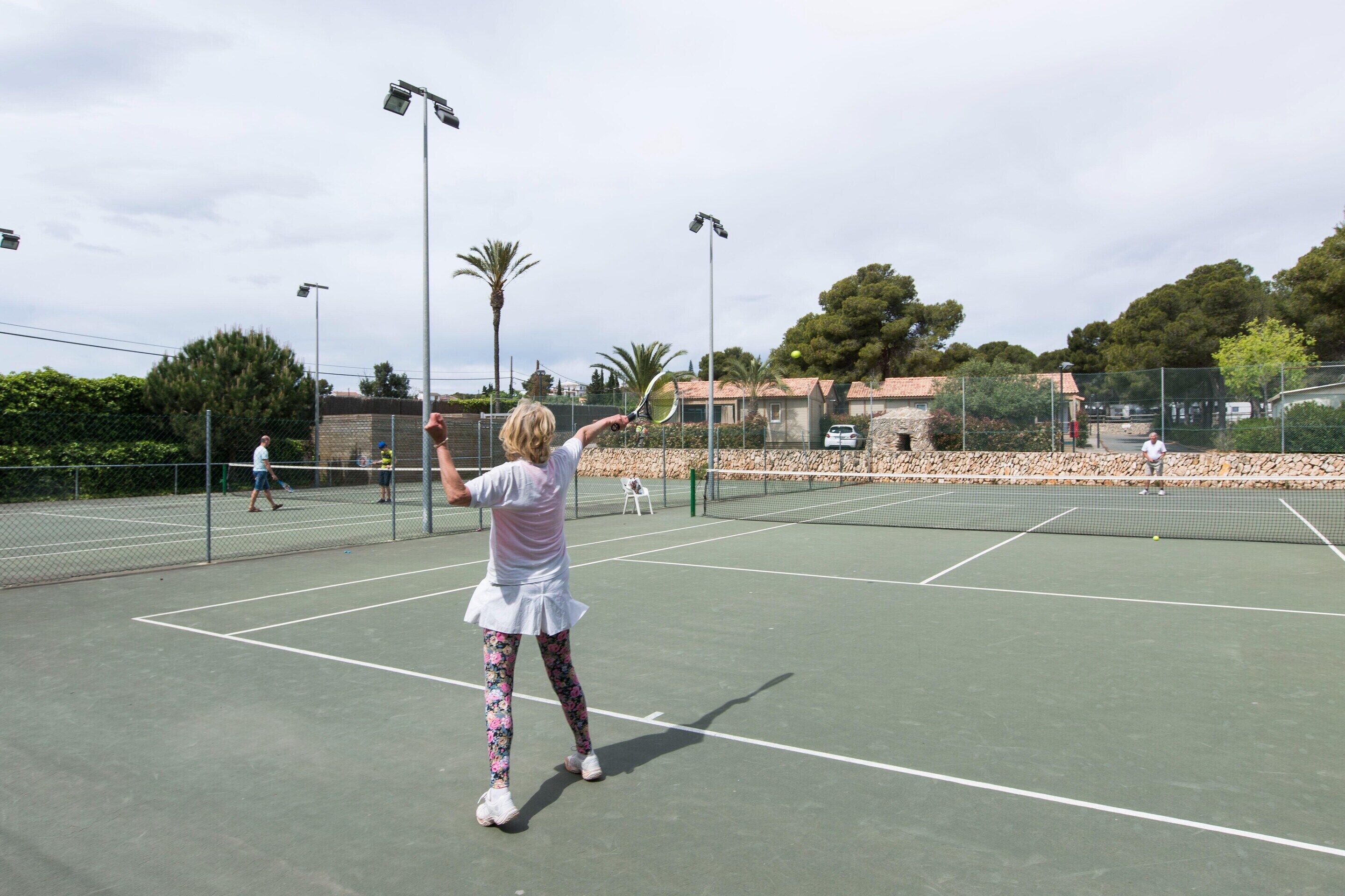 Una cancha de tenis al aire libre con red, rodeada por una valla y árboles.