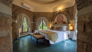 A bedroom with a stone archway, a large bed, a bench, and a view of greenery outside. - Amã Stays & Trails Kuteeram, Bangalore (Doddaballapur)