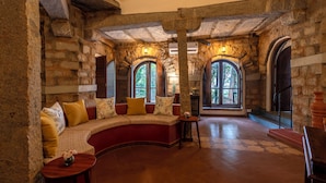 A stone-walled room with a curved sofa, a small table, and a fireplace. - Amã Stays & Trails Kuteeram, Bangalore (Doddaballapur)