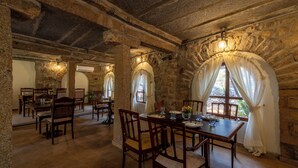 A stone-walled dining area with wooden tables and chairs, stone pillars, and arched windows with curtains. - Amã Stays & Trails Kuteeram, Bangalore (Doddaballapur)