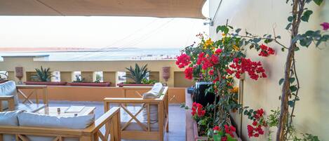 Eine Terrasse mit Holzmöbeln, Topfpflanzen und einer Kletterpflanze mit roten Blüten.
