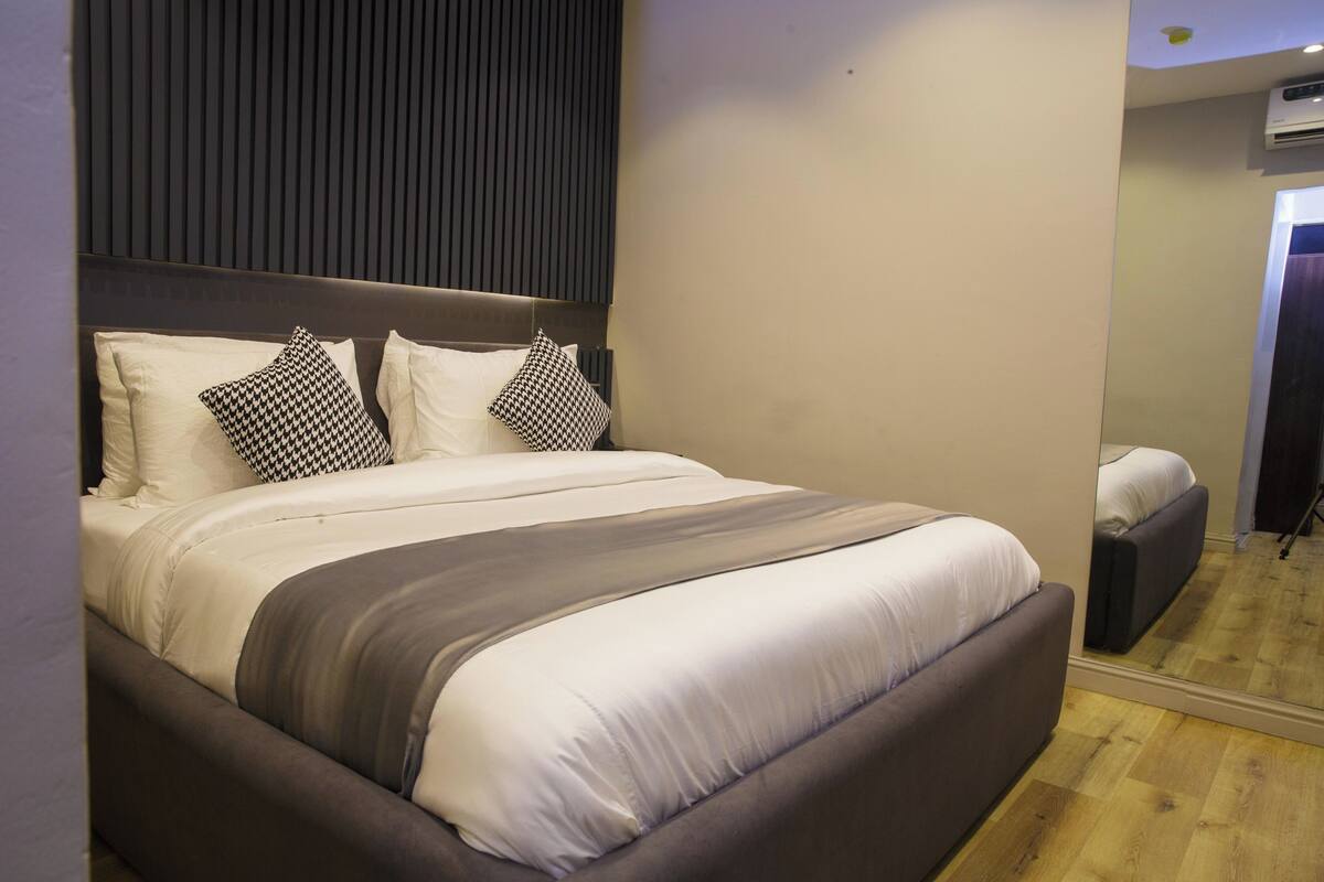 A modern bedroom with a large bed, a headboard, and a mirror.