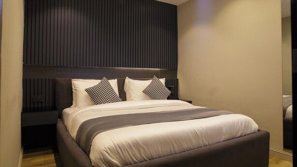 A modern bedroom with a large bed, dark headboard, and a built-in wall unit. - Mr Bay Hotel (Lagos)