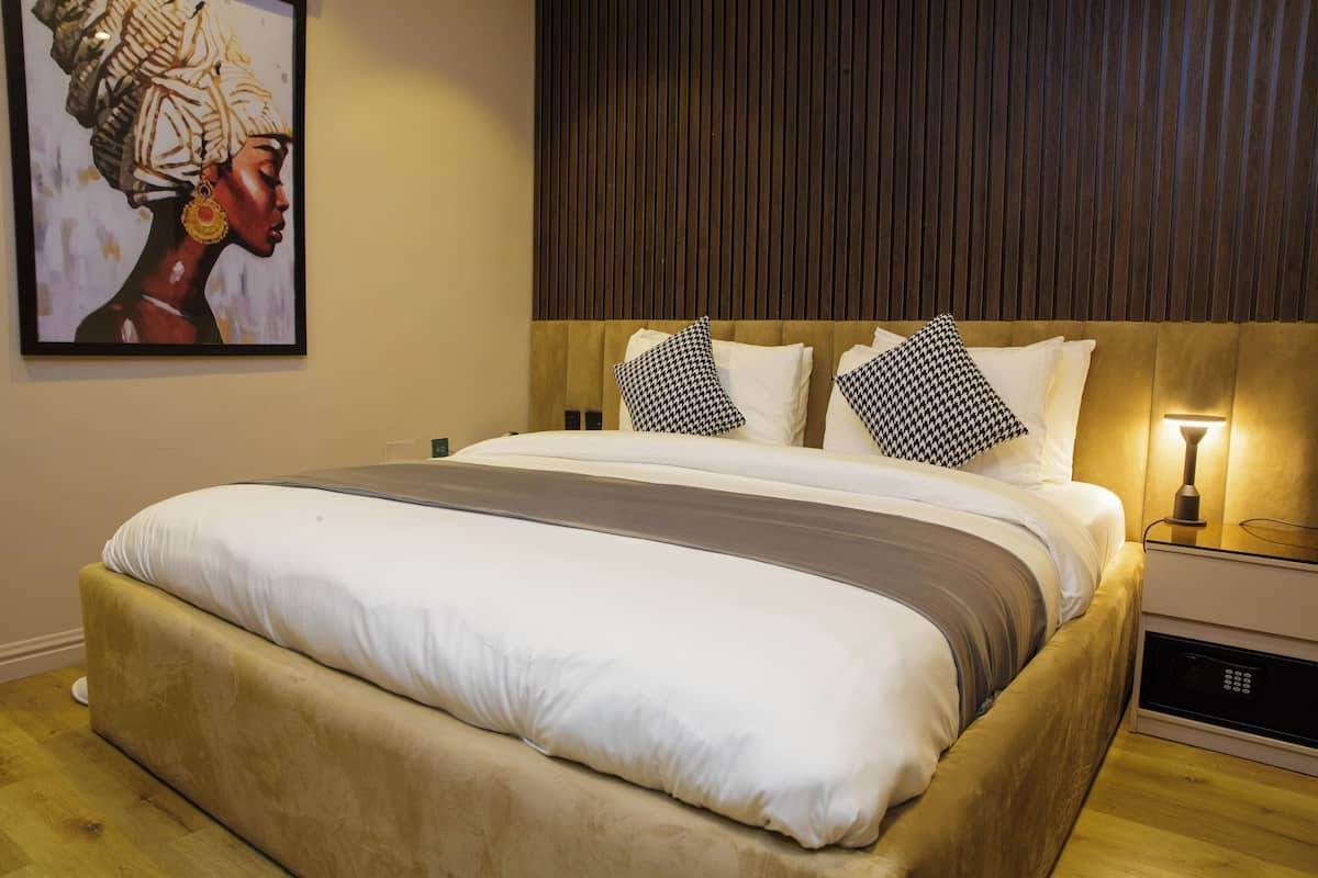 A neatly made bed with a headboard, a bedside table with a lamp, and a framed artwork on the wall.