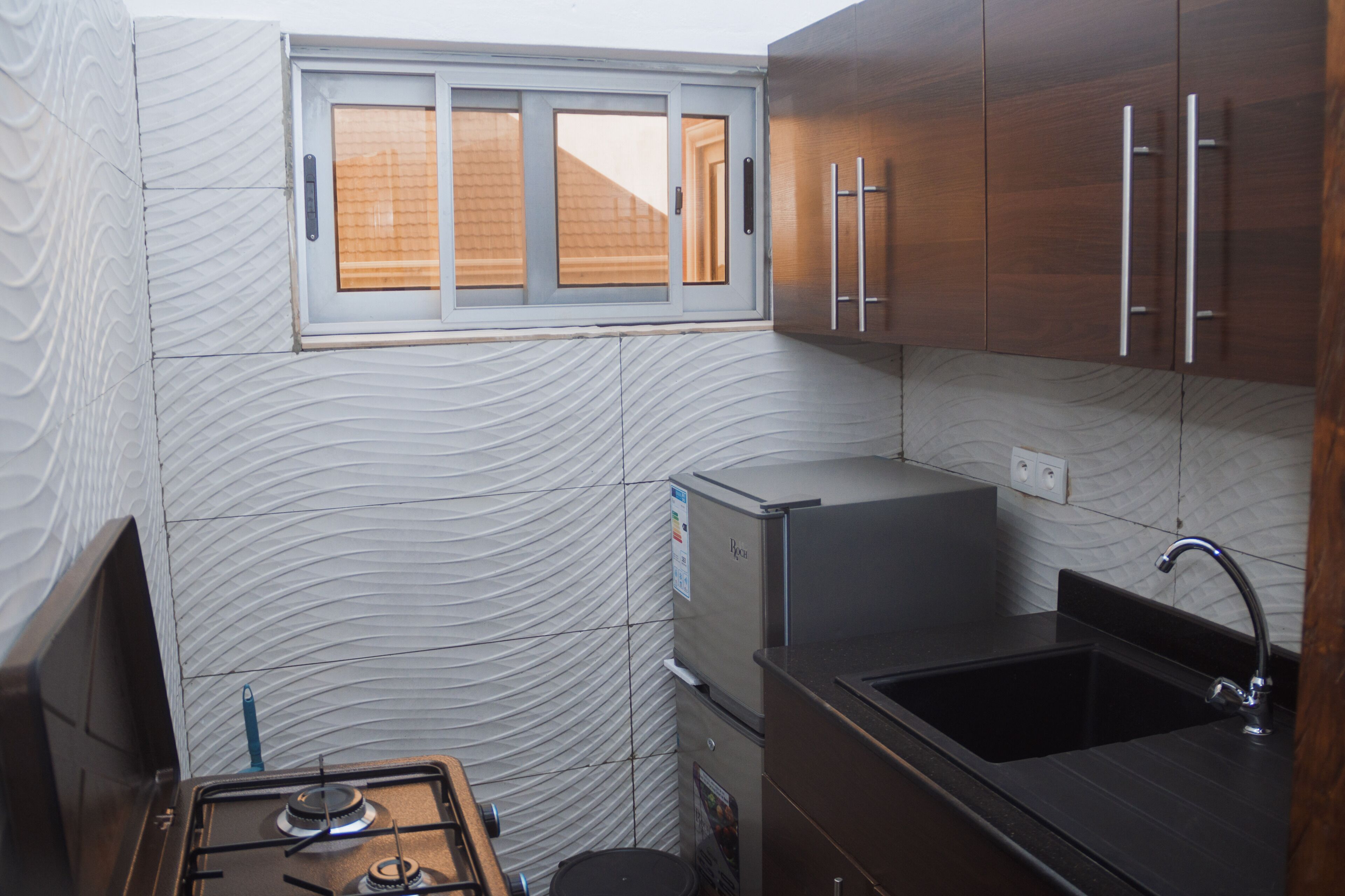 Une cuisine de taille réduite, équipée d’une cuisinière à gaz, d’un réfrigérateur, d’un évier et de meubles de rangement en bois.