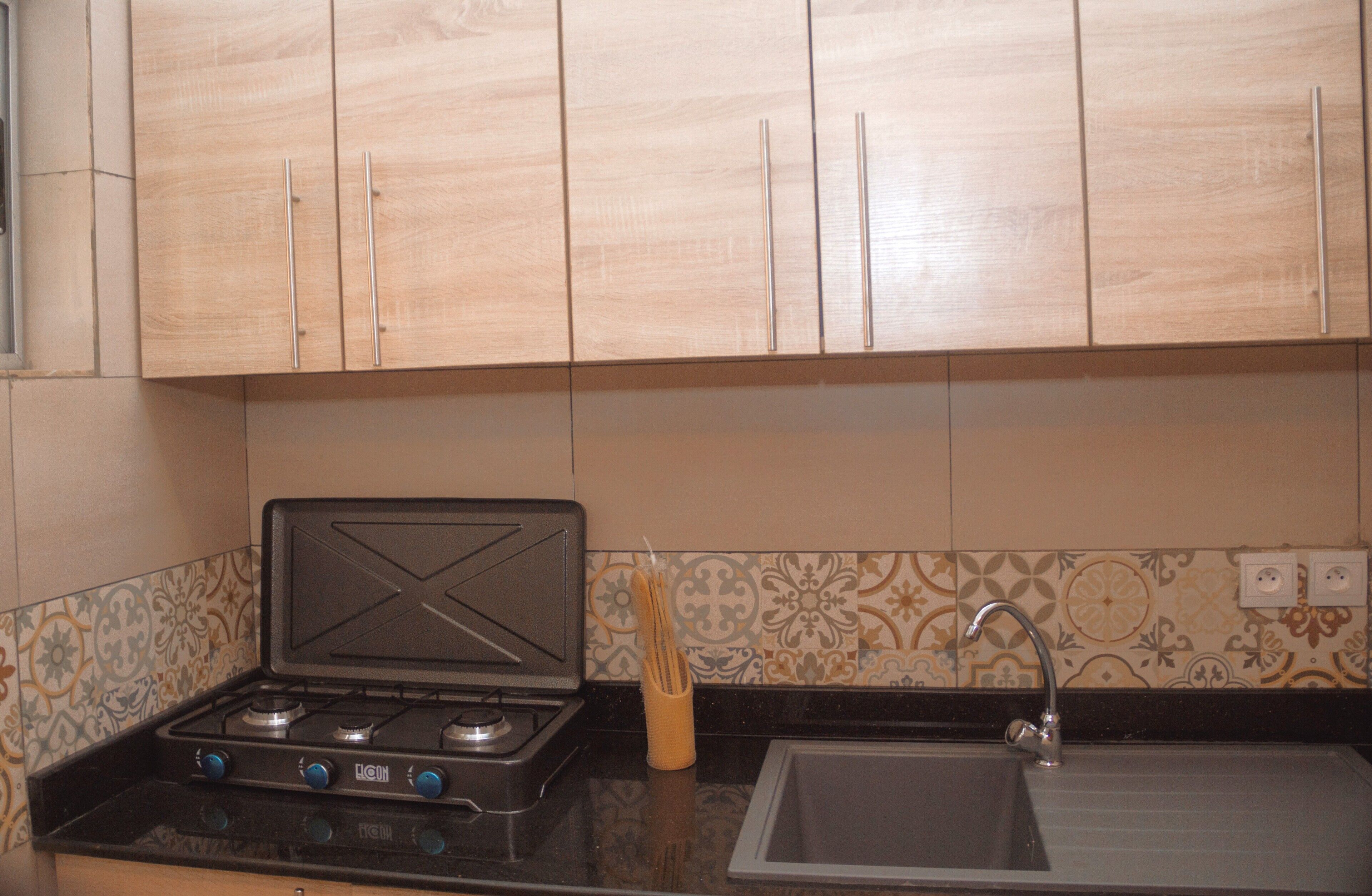 A kitchen with wooden cabinets, a gas stove, a sink, and patterned backsplash tiles.