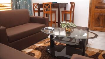 A living room with a brown sofa, a glass coffee table, and a patterned rug.