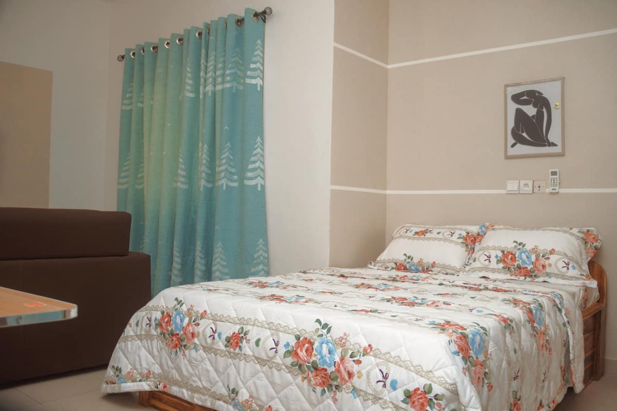 Un dormitorio con una cama, un sofá, una cortina, un cuadro y un teléfono instalado en la pared.