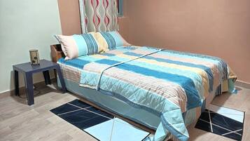 A bedroom with a bed, a nightstand, a small table, and a window with curtains.