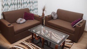 Een woonkamer met twee bruine banken, een glazen salontafel en een kamerkleed met een patroon.