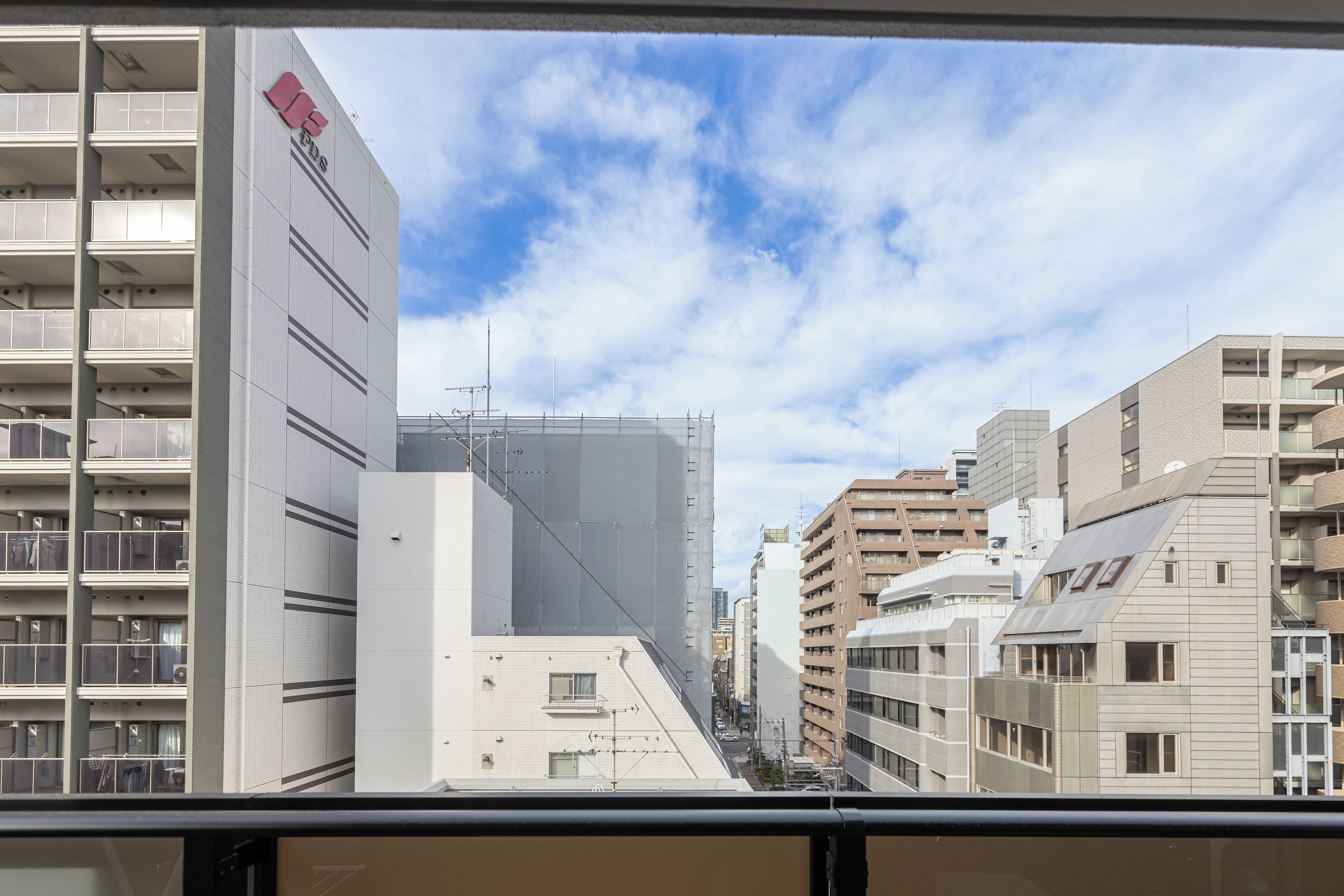 Vista de un paisaje urbano con edificios modernos, incluyendo un edificio blanco destacado con un logotipo rojo a la izquierda.