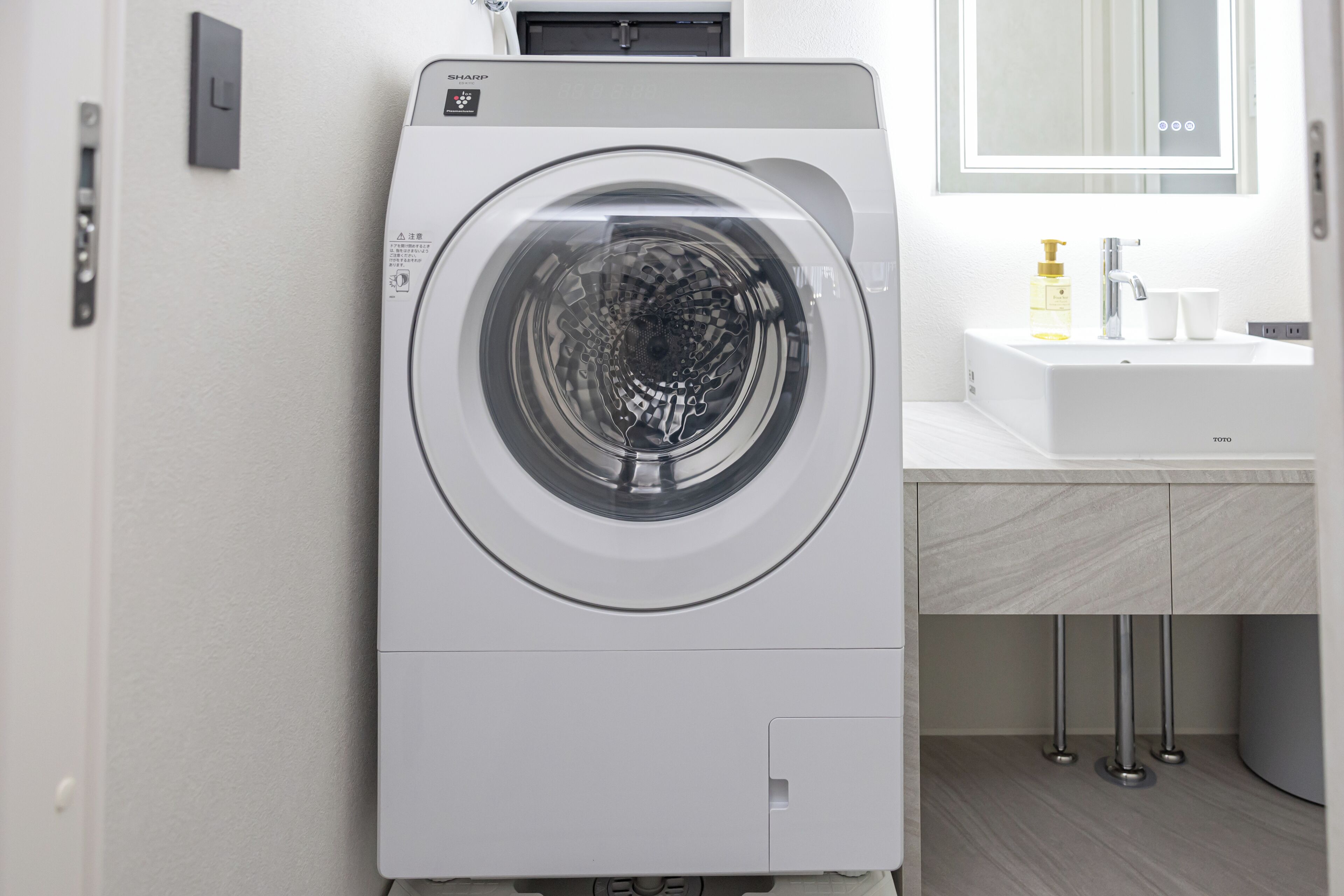 A front-loading washing machine in a modern bathroom with a sink and mirror.