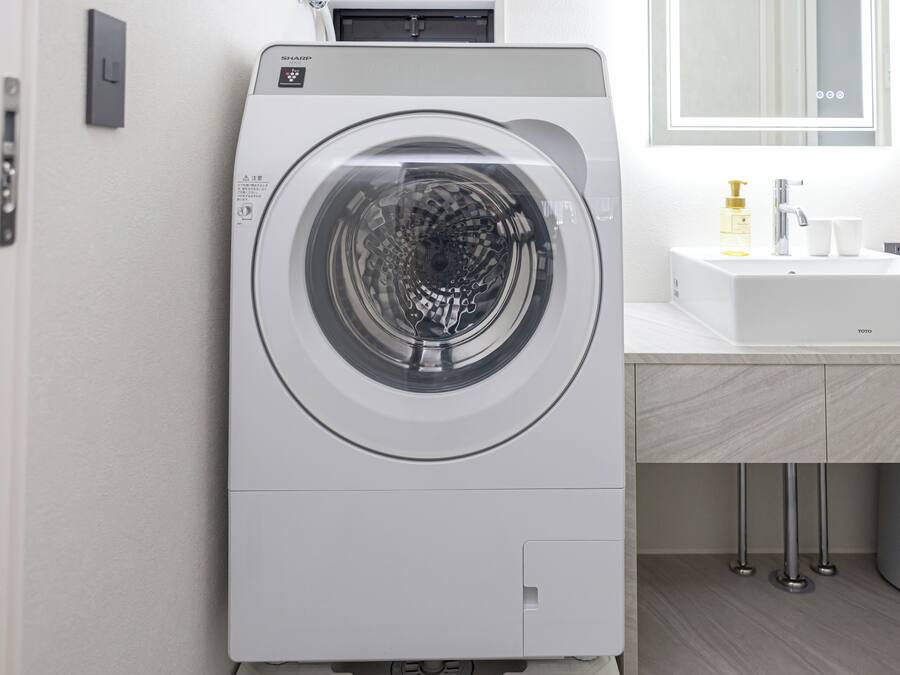 A front-loading washing machine in a modern bathroom with a sink and mirror.