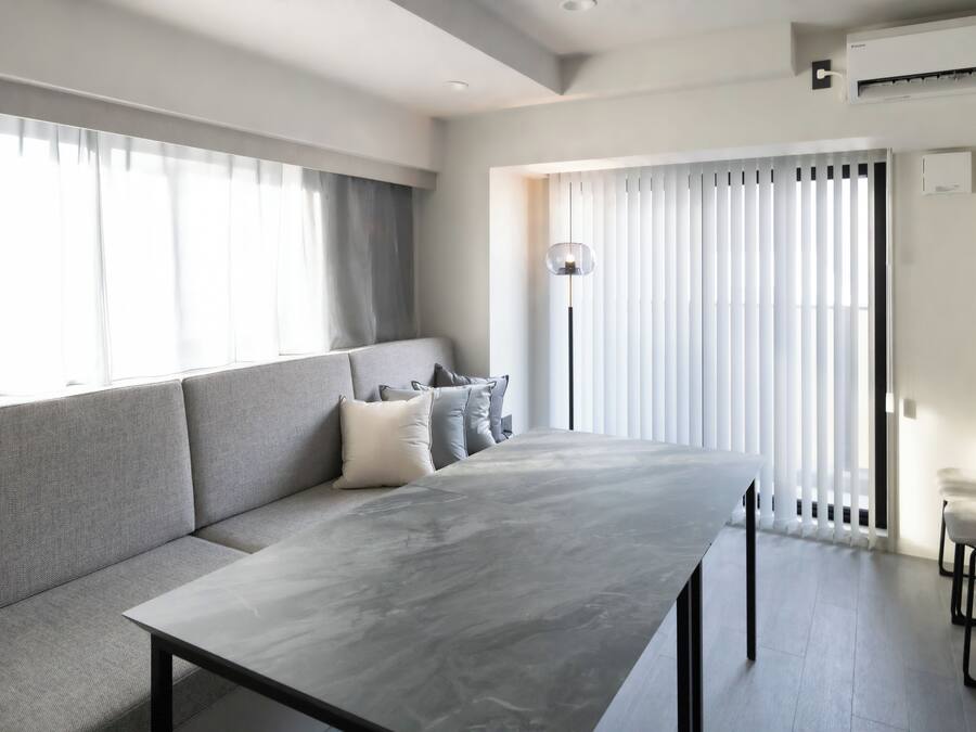 Una sala moderna con un sofá gris, una mesa larga y una lámpara de pie.