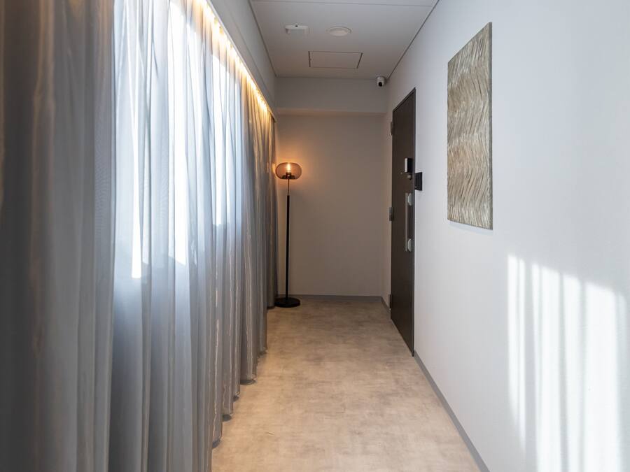 A hallway with a floor lamp, a door, and a wall-mounted artwork.