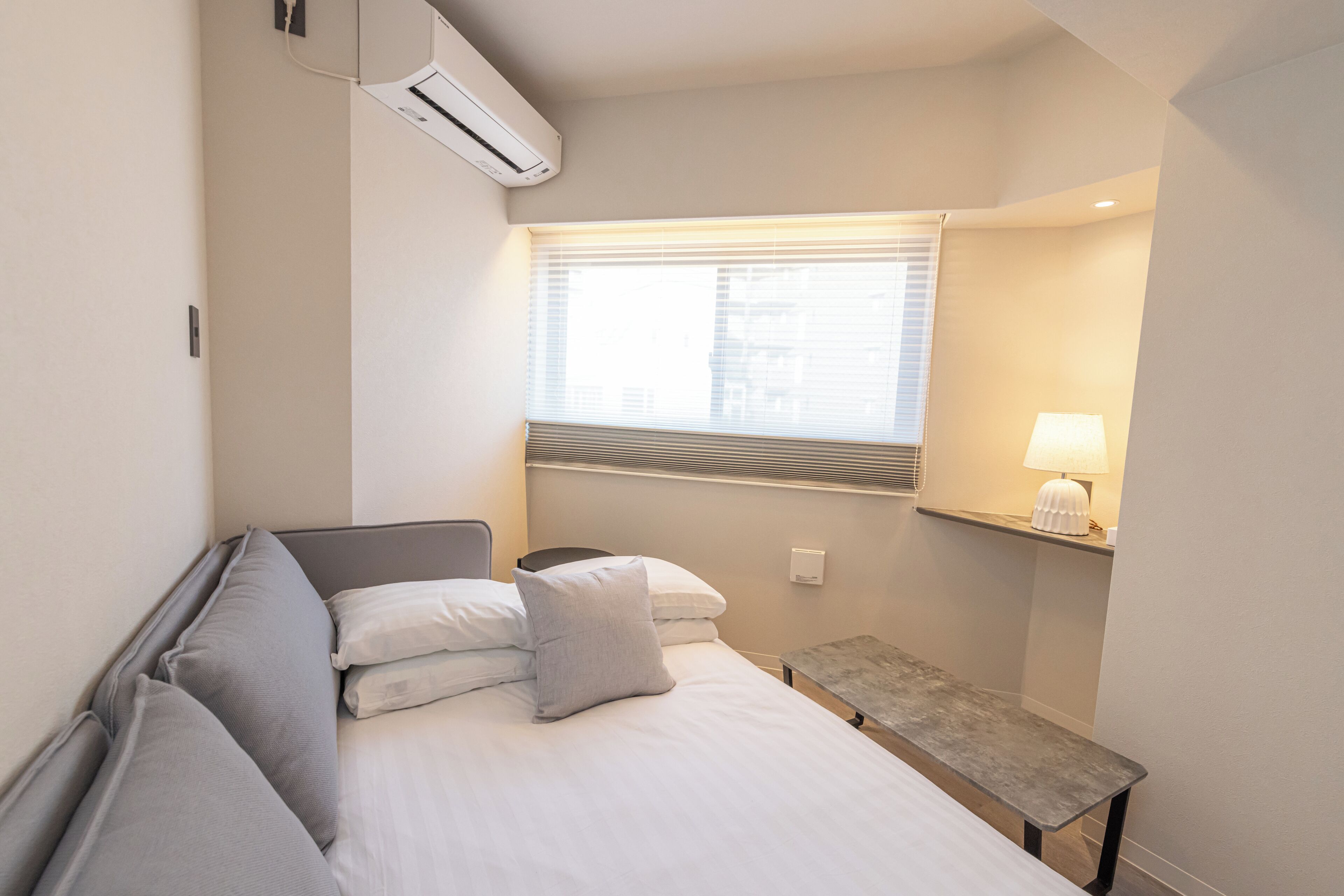 Une chambre d’hôtel avec un lit, une table de chevet, une lampe et une fenêtre avec des stores.