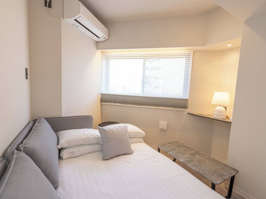 Una habitación de hotel con una cama, una mesita de noche, una lámpara y una ventana con persianas.